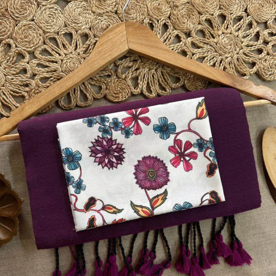 A folded plum saree with tasselled ends, its floral-print blouse piece on top, over a wooden hanger